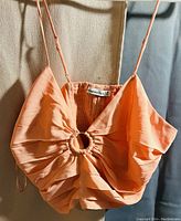 Front view of the peach satin-like spaghetti strap top with a circular ring detail in the center and gathered fabric design.
