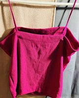 Photo of bright pink ribbed crop top with off-shoulder short sleeves and thin spaghetti straps hung on a hanger.