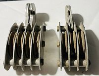 Overhead view of two four-wheel metal pulleys side by side, showing construction and wheel details