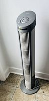 Full view of the tower fan showing its height, base, and grille design, in grey and white.