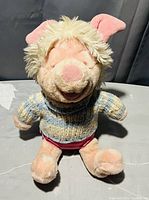 Photo of the vintage Piglet plush with pink fur and cream tuft on head wearing a knitted sweater and red shorts.