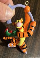 Close-up photo of vintage Tigger Christmas tree ornament being held, showing details of the figurine and hanging loop.