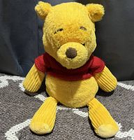 Front-facing image of Winnie the Pooh plush toy sitting upright on carpeted floor with dark background.