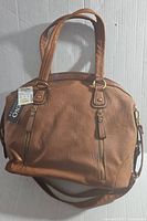 Front view showing brown leather handbag with two handles, gold-tone zipper accents, and tags attached.