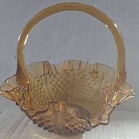 Side angle photo showing the amber translucent hobnail glass basket with ruffled edges and fixed handle.