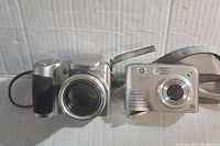 Two cameras side by side, showing full front and some lens and strap details.