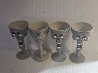 Four gray plastic Halloween goblets with scary skull and face designs photographed on a white background.