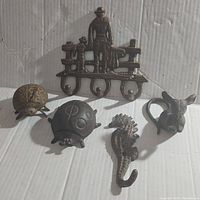 Overview of six assorted cast iron pieces including a wall hook with man and dog, two ladybug shapes, seahorse hook, and mouse figurine.