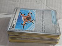 Stack of assorted Pokémon cards with Delivery Drone card on top, showing artwork of an orange drone on blue background.