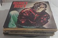 Photo showing a stack of vinyl record covers with Quiet Riot Metal Health on top, depicting a masked character in a red leather outfit.