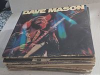 Stack of vintage vinyl record albums with Dave Mason album on top showing wear on cover edges.
