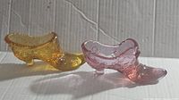Pair of amber and pink Fenton glass shoes shown from side angle on corrugated cardboard background.