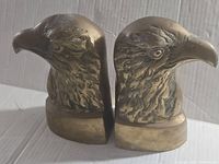 Pair of vintage brass eagle bookends shown from front angle on a white surface with shadows visible.