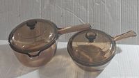 Pair of amber tinted vintage Pyrex Vision glass saucepans, one larger and one smaller, each with lid and handle.
