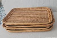 Four stacked rectangular trays made of bamboo, wicker, and rattan on a white surface.