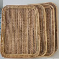 Four stacked vintage bamboo, wicker, and rattan trays showing woven bases and rounded bamboo frames.