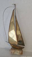 Full front view of vintage metal sailboat sculpture showing the full height, metal sails, and stone base.