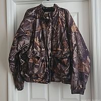 Front view of the vintage Woolrich camouflage hunting jacket hanging on a door showing full jacket with pockets and elastic cuffs.