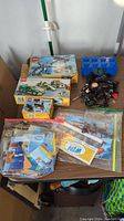 Overview of multiple boxed LEGO sets, loose LEGO parts in bags, and plastic figurines on a table.