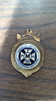 Front of antique brass and enamel keychain showing PFMA emblem and dates