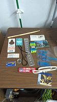 Photo of entire lot displayed on wood table, showing drumstick, door hanger, assorted cards, metal tongs, plastic bags, and other small items.