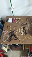 Wide view of various costume jewelry items spread on table including necklaces, bracelets, rings, earrings, charms, and watch bands.