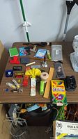 Desk drawer lot contents on table showing various office supplies, small tools, and novelty items.