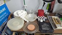 Photo of various kitchen items on table including plastic serving trays, bowls, utensils, and pans.