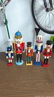 Five wooden nutcrackers displayed side by side on a wooden floor beneath a bicycle wheel.