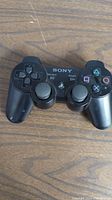 Front view of black Sony PS3 controller showing buttons, analog sticks, and brand name.