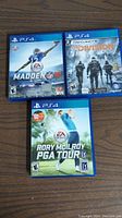 Photo showing three PlayStation 4 game cases for Madden NFL 16, Tom Clancy's The Division, and Rory McIlroy PGA Tour on a wooden floor.