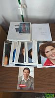 Photo showing multiple headshot photos laid out on a table along with two binders containing scripts.