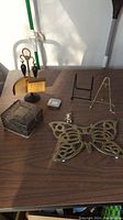 Overview photo of all metal items on a wooden table showing variety including trivet, fireplace tools, trays, stands, and box.