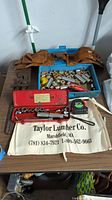 Overview of the tool lot showing red socket wrench set, tape measure, various brass fittings in a blue tray, and two brown leather tool belts.