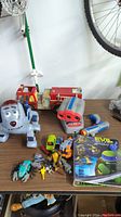 Wide photo of all toys including fire truck, robot dog, toy cars, figures, binoculars, and TMNT comic book on a table.
