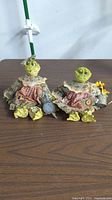 Two ceramic frog decorations with detailed fabric clothing and gardening accessories on table