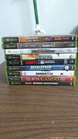 Stack of original Xbox game cases showing titles including Star Wars The Clone Wars, Tom Clancy Rainbow Six 3, Need for Speed Underground 2, Battlefield 2, ESPN Baseball, Madden 06, Bicycle Casino, and Cabela's Outdoor Adventures.