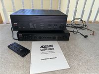 Adcom GSP-560 surround sound processor/amplifier with GFP-555II preamplifier, remote control, and owner's manual on floor.