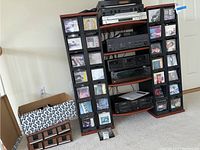 Photo showing CDs and cassette tapes displayed on black racks alongside audio equipment stand with several components.