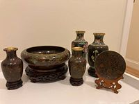Photo of all six items including 4 cloisonné jars, 1 bowl, 1 small plate on wooden stand, arranged together showing form and decoration.