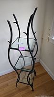 Full view of shelving unit showing black metal vine-like legs with leaves and square glass shelves
