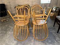 Six wooden dining chairs stacked seat down showing legs and spindles