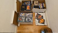 Top view showing three bankers boxes filled with DVDs and some DVDs placed beside, revealing multiple movie titles and collections.