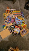 Overview of collection of young kids puzzles including framed puzzles, boxed puzzles, and wooden peg puzzles scattered on a concrete floor.