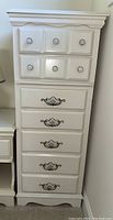 Front view of the white lingerie dresser showing seven drawers with floral handles on the bottom and round knobs on top drawers.