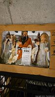 Three ceramic figurines in original box packaging showing Fu Xing, Lu Xing, and Shou Xing with a price tag and handwritten note describing them as 3 figurines representing Prosperity, Longevity, and Luck.