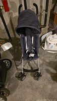 Front view of dark fabric Maclaren umbrella stroller showing padded harness, canopy, and dual front wheels.