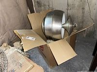 MCM metal arching lamp shade and arm placed inside a cardboard box within a storage setting.