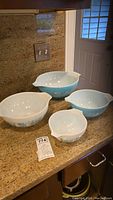 Four vintage Pyrex Amish Butterprint nesting mixing bowls arranged on kitchen counter labeled with lot number.