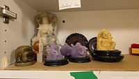 Shelf view showing multiple stone figurines of Asian religious icons in various colors and wooden stands.